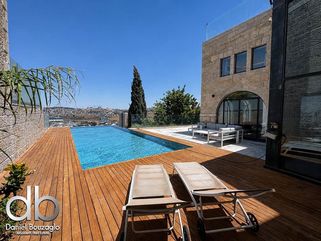 Luxurious rooftop pool deck with a rectangular pool, wooden decking, and two sun loungers facing a city view and glass railing.