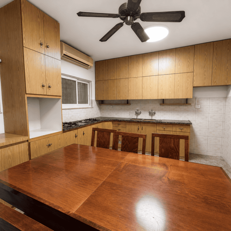 Wooden kitchen with tall cabinets, a large wooden dining table in the foreground, gas stove, and ceiling fan.