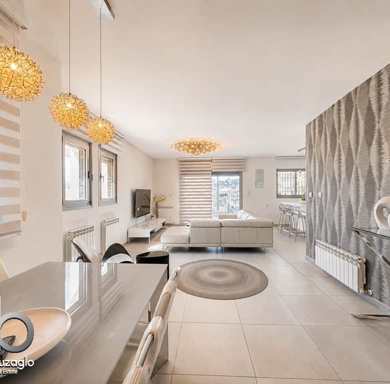 Open-concept living and dining area with white furniture, woven pendant lights, and a textured gray feature wall.