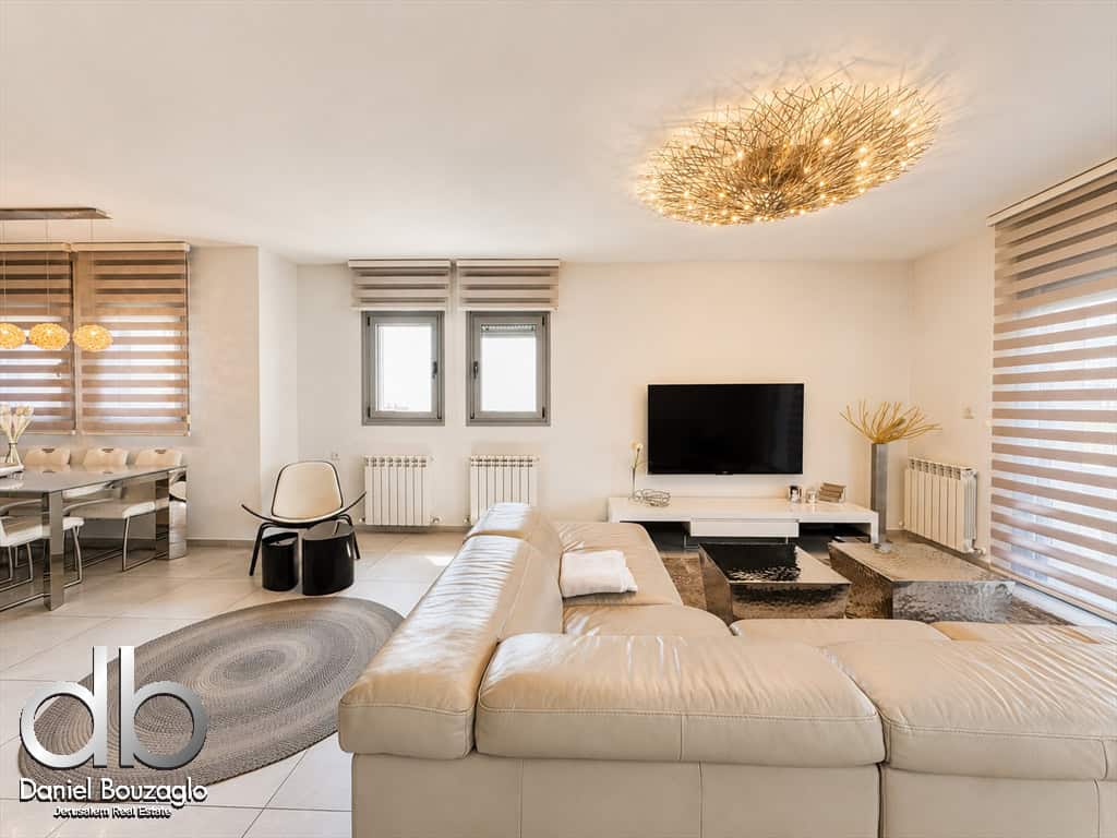 Bright modern living room with a beige sectional, circular gray rug, and a sunburst chandelier above.