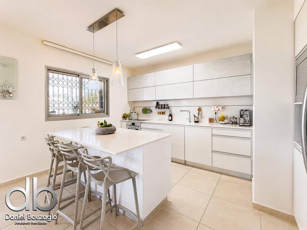 Bright, modern kitchen with a white island and four grey bar stools under pendant lights