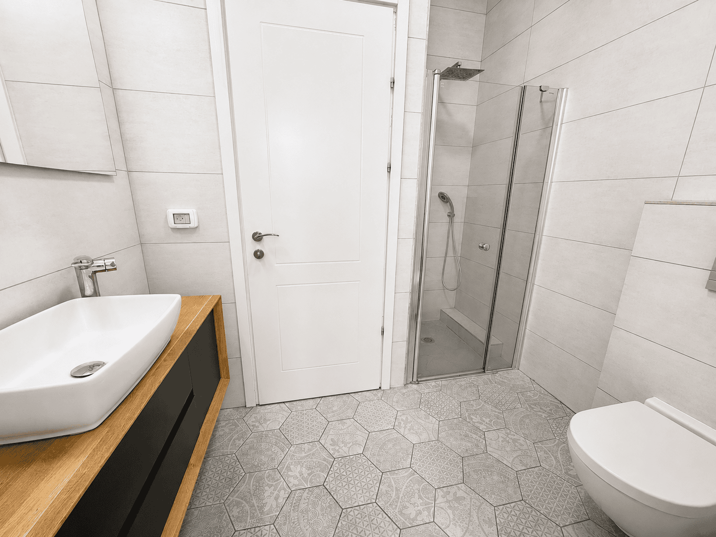 White rectangular vessel sink on a wooden vanity with black cabinet doors against tiled walls in a modern bathroom.